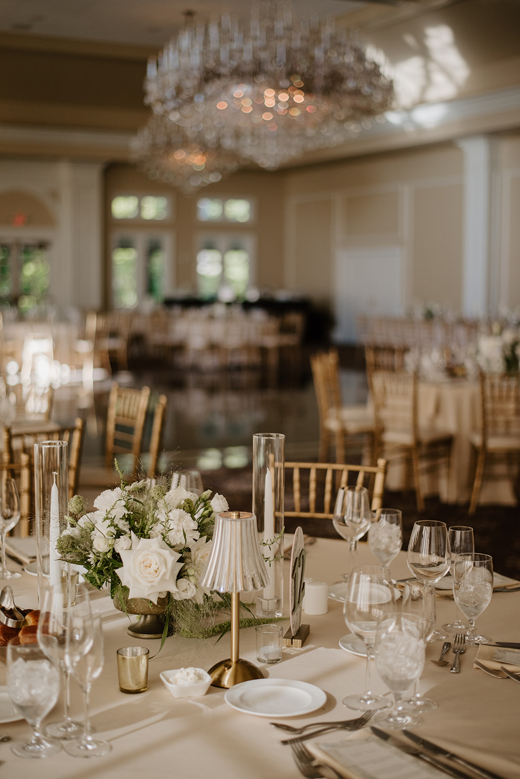 A beautifully decorated reception table in a grand hall with crystal chandeliers hanging in the background.
